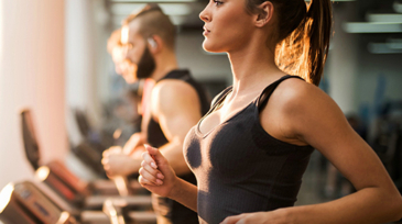 Young people exercising in a gym on treadmill. Focus is on foreground.